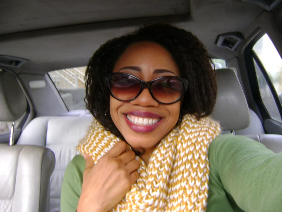 E.C. Scott, smiling, seated in a car in sunglasses and a knitted scarf
