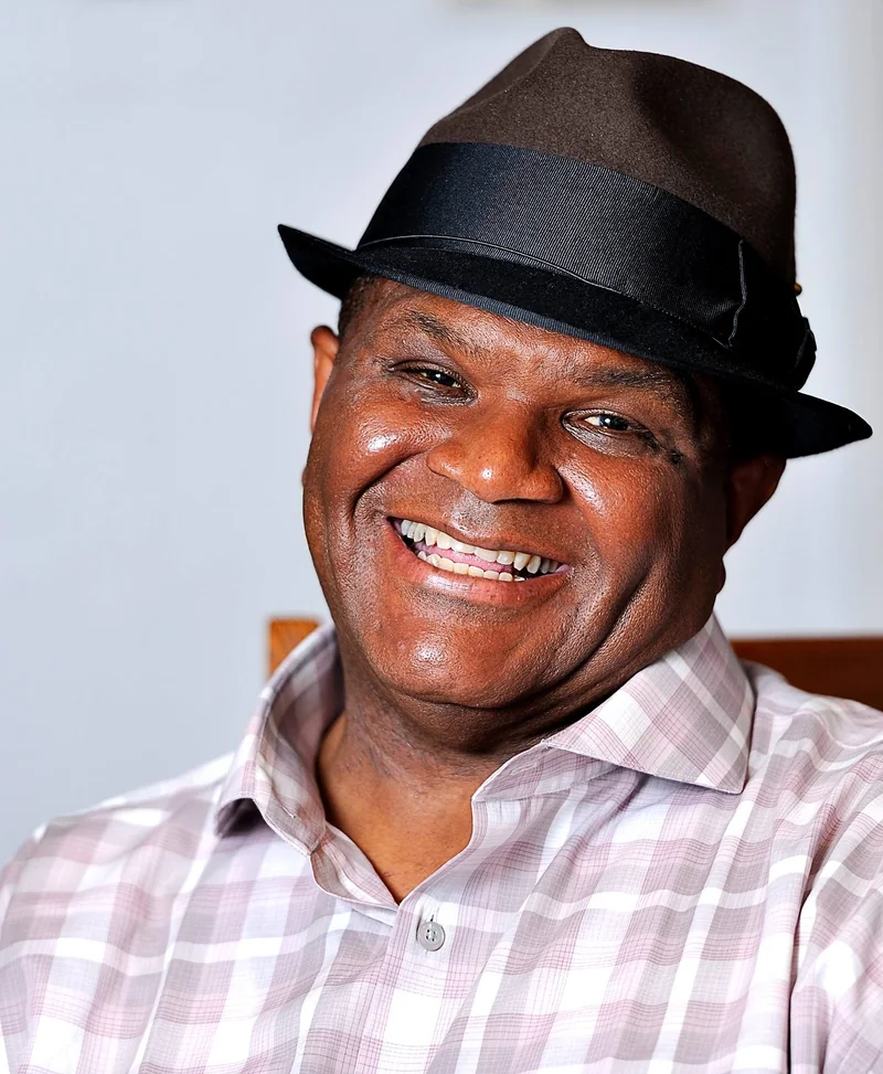 Larry Batiste in a dark fedora and checked shirt, smiling