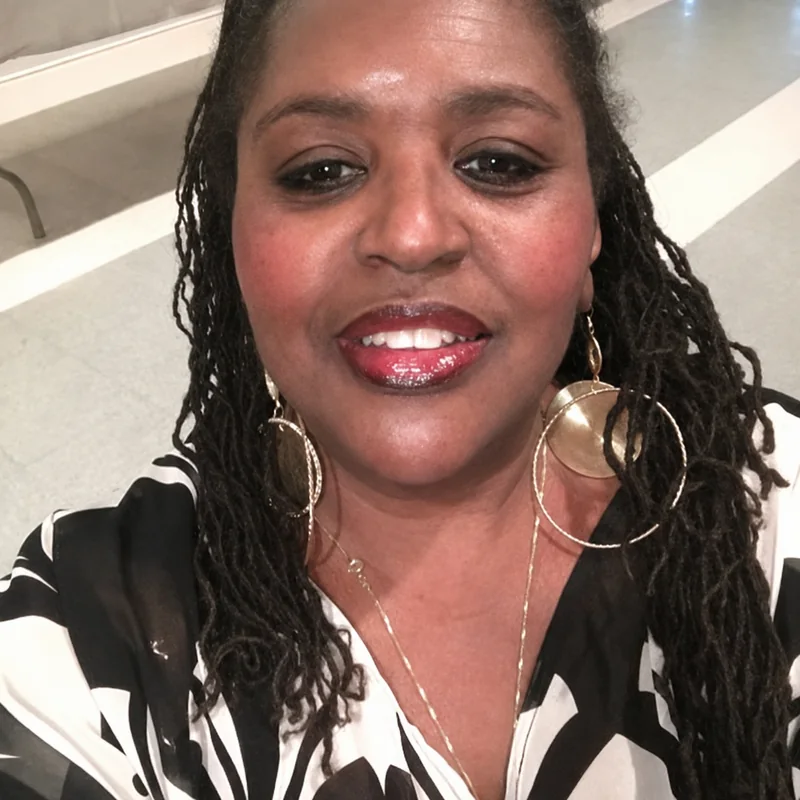 Sue McCracklin, smiling, with long locs and gold hoop earrings