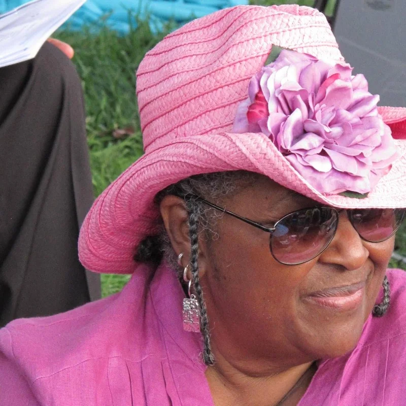 Velma Landers, in a pink hat with a flower, wearing sunglasses